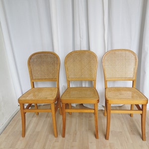 May include: Three wooden chairs with cane seats and backs. The chairs are light brown and have a simple design.