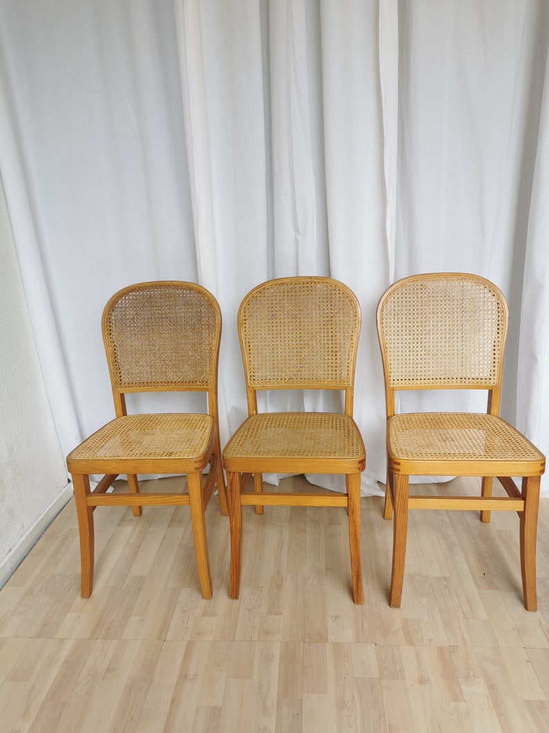 May include: Three wooden chairs with cane seats and backs. The chairs are light brown and have a simple design.