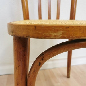May include: A close-up of a wooden chair with a woven cane seat. The chair is made of light brown wood and has a simple, classic design.