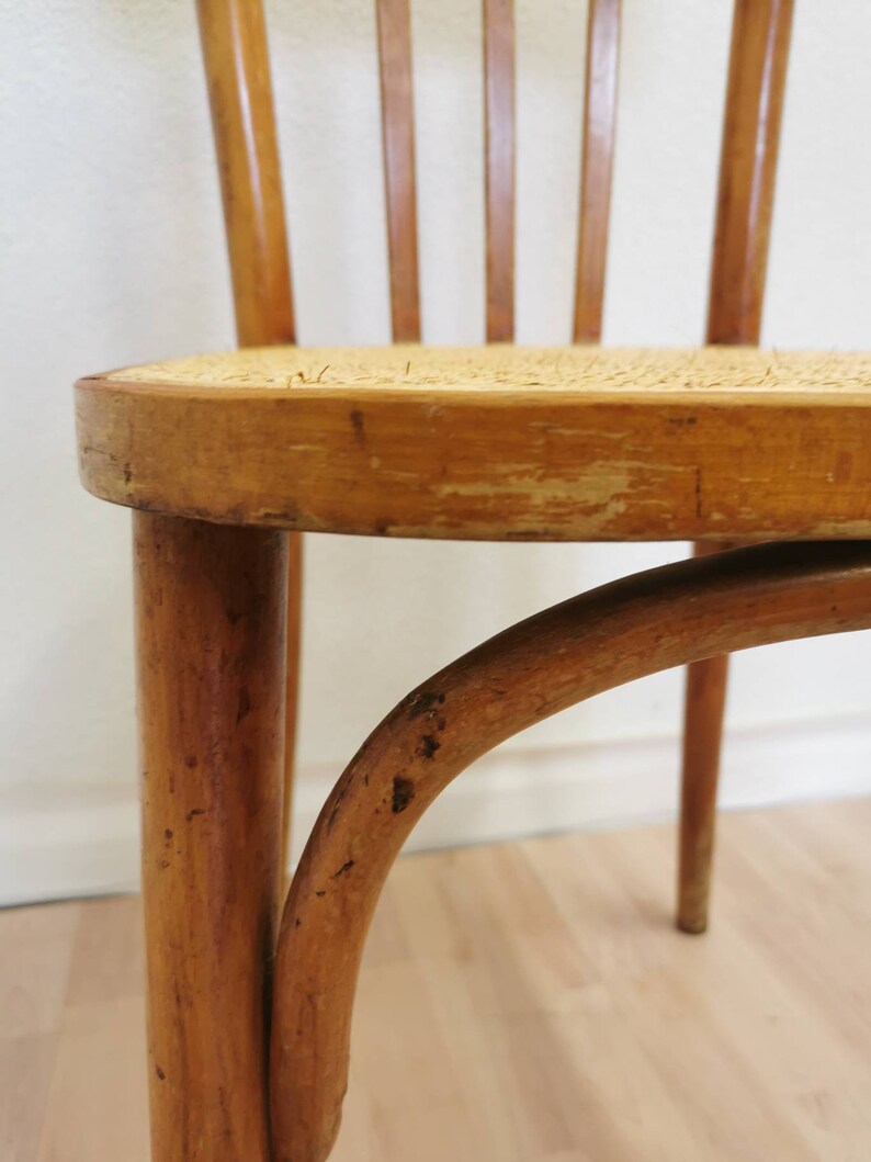 May include: A close-up of a wooden chair with a woven cane seat. The chair is made of light brown wood and has a simple, classic design.