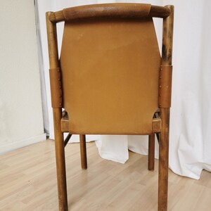 May include: A brown leather chair with a wooden frame. The chair has a simple design with a high back and four legs.