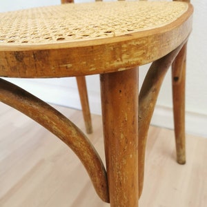 May include: Close-up of the bottom of a wooden chair with a woven cane seat. The chair has a light brown finish and shows signs of wear and tear.