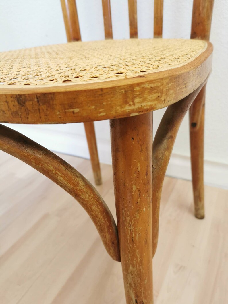 May include: Close-up of the bottom of a wooden chair with a woven cane seat. The chair has a light brown finish and shows signs of wear and tear.