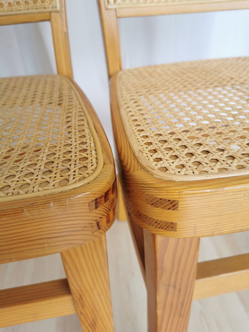 May include: Two wooden chairs with woven cane seats. The chairs are made of light wood and have a simple design.