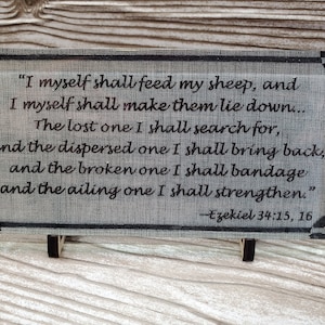 May include: A gray wooden plaque with a black border and black text. The text reads "I myself shall feed my sheep, and I myself shall make them lie down... The lost one I shall search for, and the dispersed one I shall bring back, and the broken one I shall bandage and the ailing one I shall strengthen." - Ezekiel 34:15, 16