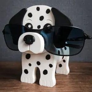 May include: A wooden Dalmatian dog ornament, white with black spots, wearing black sunglasses. The dog has a black nose and ears. The word "TIMUX" is printed on the bottom right of the ornament.
