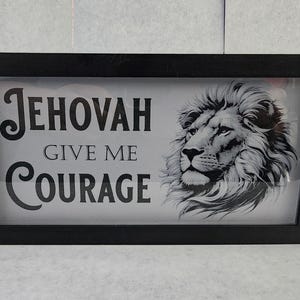 May include: Black framed artwork with the text "JEHOVAH GIVE ME COURAGE" and a grayscale image of a lion's head. The artwork is rectangular and appears to be a print or a photograph.