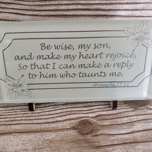May include: A white glass plaque with a black border and floral design. The plaque features a quote from Proverbs 27:11, "Be wise, my son, and make my heart rejoice, So that I can make a reply to him who taunts me."