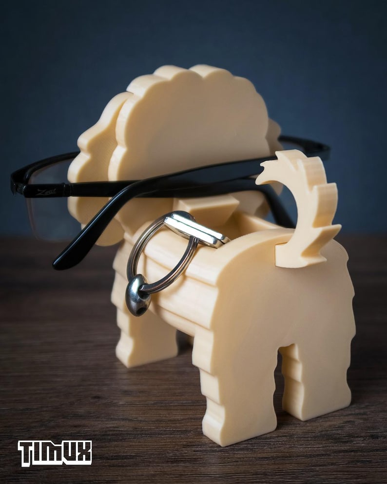 May include: A cream-colored, dog-shaped organizer made of layered material, featuring a slot for holding eyeglasses across the head and a small compartment for keys or accessories. The word TIMUX is printed in white at the bottom left corner.