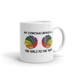May include: White ceramic mug with a black graphic that says "My conchas bring all the girls to the yard". The graphic also features two colorful conchas, a type of Mexican sweet bread.