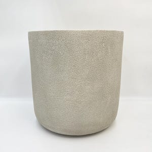May include: A large, light grey, textured ceramic planter. The planter has a rounded bottom and a wide, cylindrical shape.
