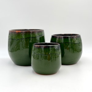 May include: Three green ceramic pots with a brown glaze. The pots are different sizes and are arranged in a row from largest to smallest.