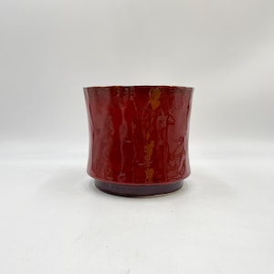 May include: A red ceramic planter with a slightly flared rim and a textured surface.