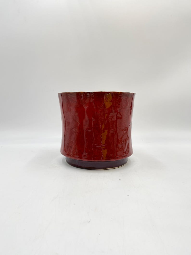 May include: A red ceramic planter with a slightly flared rim and a textured surface.