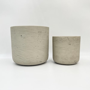 May include: Two concrete planters, one larger than the other, with a textured surface. Both planters are a light grey colour.