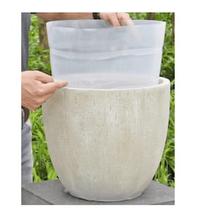 Op de afbeelding: Een beige, getextureerde keramische plantenbak met een doorzichtige plastic voering die wordt ingebracht. De plantenbak heeft een afgeronde vorm en een ruwe, verticaal gestreepte textuur. De voering is flexibel.
