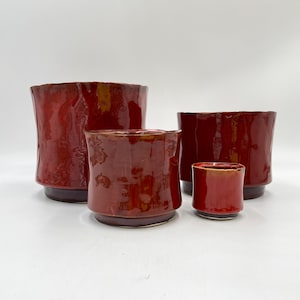 May include: Four red ceramic planters of varying sizes. The planters are all a deep red color with a slightly textured finish.