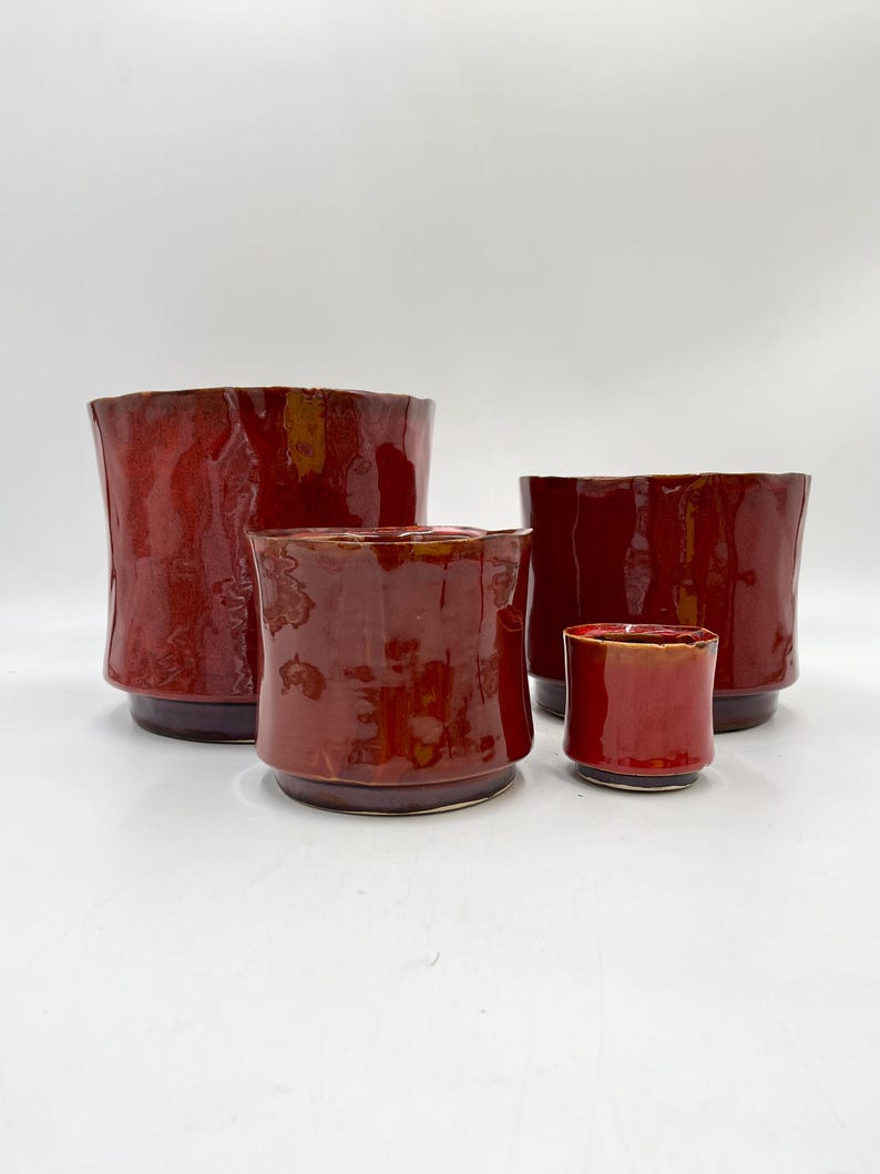 May include: Four red ceramic planters of varying sizes. The planters are all a deep red color with a slightly textured finish.