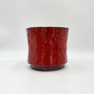 May include: A red ceramic planter with a textured surface. The planter has a slightly flared rim and a rounded base.