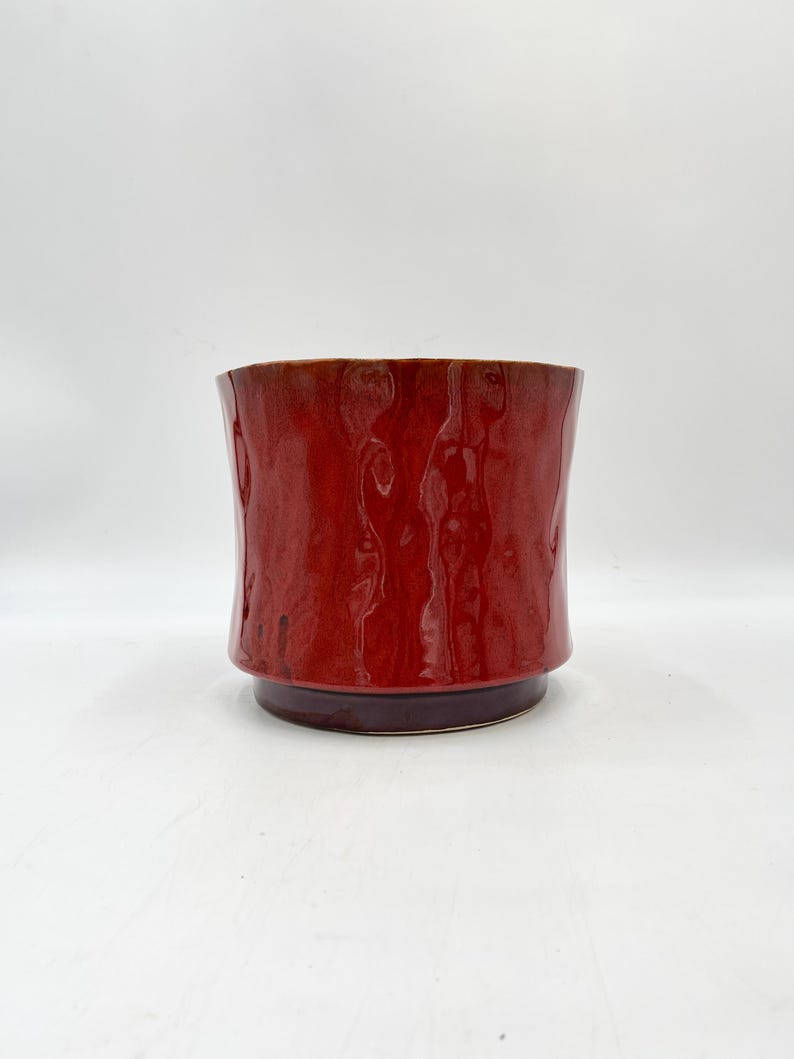May include: A red ceramic planter with a textured surface. The planter has a slightly flared rim and a rounded base.