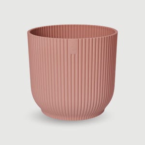 May include: A blush pink, ribbed planter with a rounded base. The cylindrical pot has vertical grooves and a small logo on the side. This decorative planter is suitable for indoor or outdoor use.