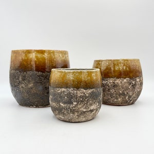 May include: Three ceramic planters in different sizes, with a speckled brown and yellow glaze. The planters are round and have a slightly flared lip.