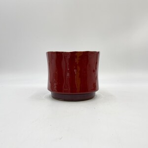 May include: A red ceramic planter with a slightly flared rim and a dark purple base.