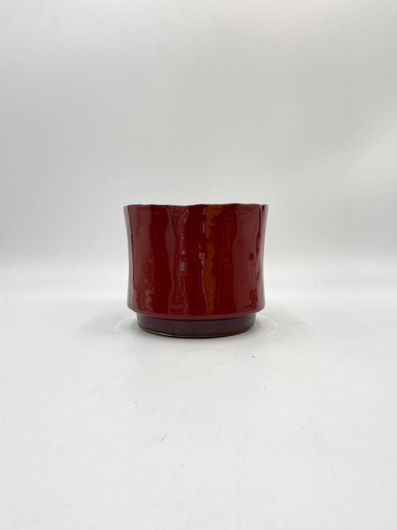May include: A red ceramic planter with a slightly flared rim and a dark purple base.