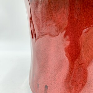 May include: A large, red ceramic planter with a glossy finish. The planter has a unique, wavy shape and a subtle brown glaze.