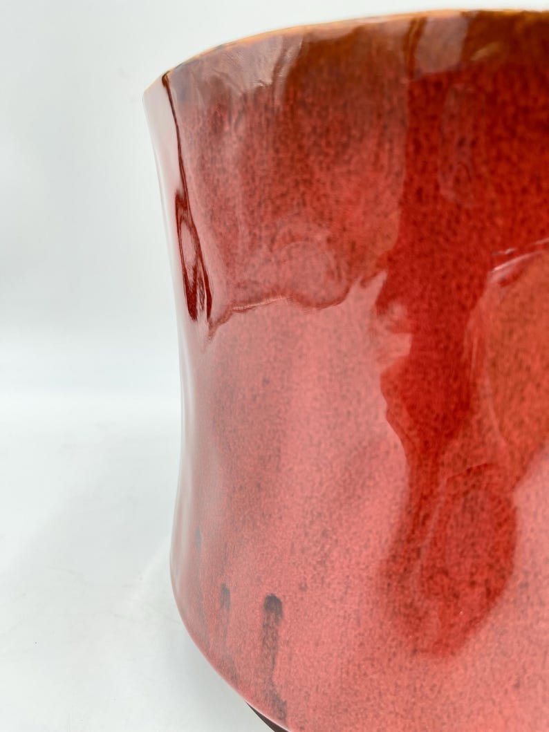 May include: A large, red ceramic planter with a glossy finish. The planter has a unique, wavy shape and a subtle brown glaze.