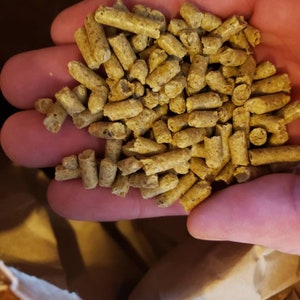 May include: A handful of small, brown, cylindrical pellets. The pellets are made of compressed wood and are used as fuel for a wood-burning stove.