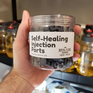 Puede incluir: Un frasco de plástico transparente lleno de 100 puertos de inyección autocurativos negros para uso micológico. El frasco tiene una etiqueta blanca que dice "Self-Healing Injection Ports" y "Royal Flush Mushrooms 100 PCS".
