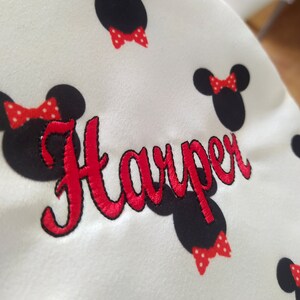 May include: White fabric with red and black embroidered Mickey Mouse ears and a red bow. The name "Harper" is embroidered in red cursive lettering.