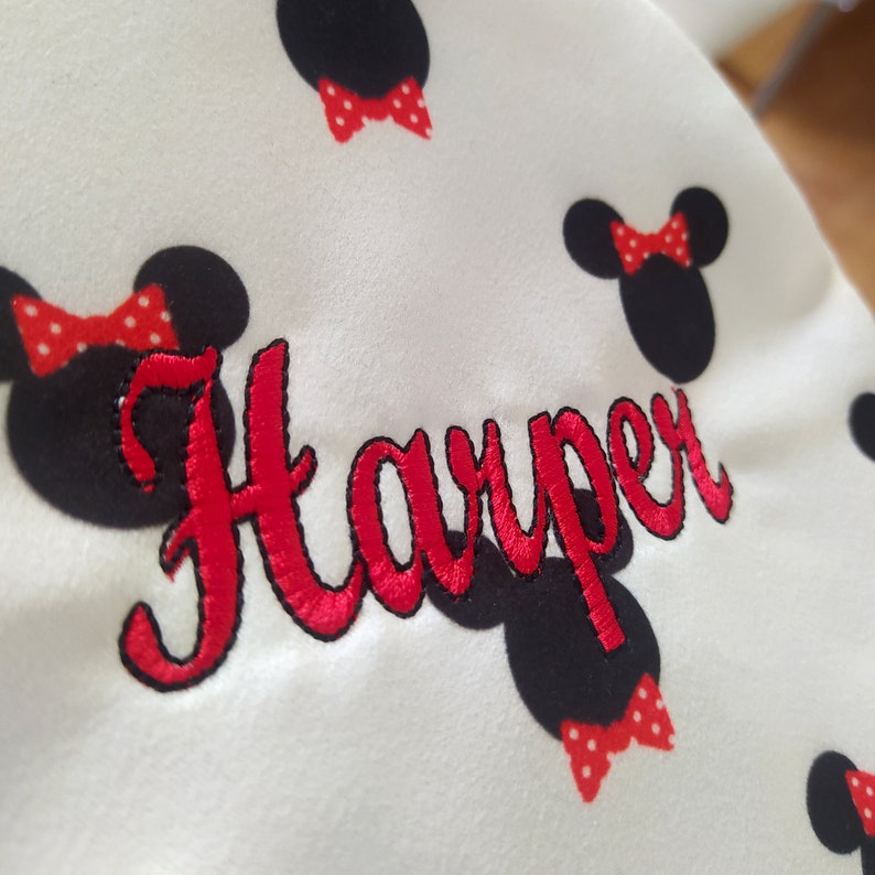 May include: White fabric with red and black embroidered Mickey Mouse ears and a red bow. The name "Harper" is embroidered in red cursive lettering.
