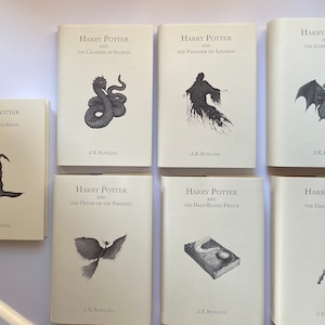 May include: A collection of seven hardcover books from the Harry Potter series by J.K. Rowling. Each book features a unique black and white illustration on the cover, including a sorting hat, a snake, and a phoenix.