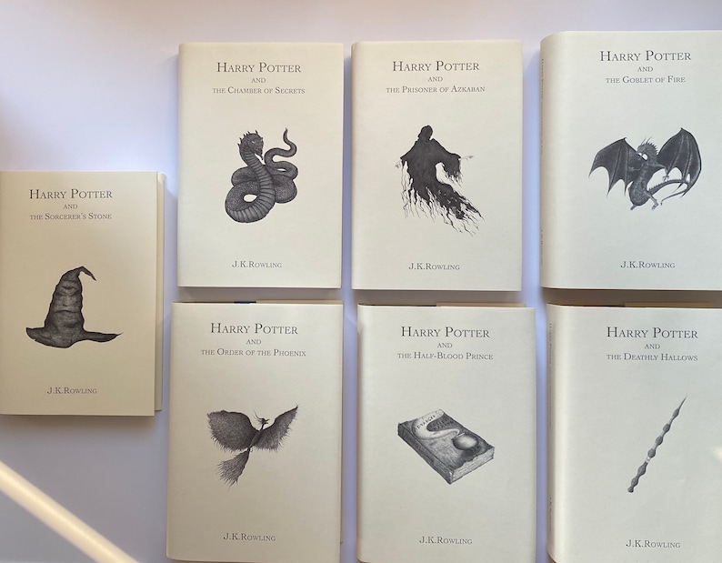 May include: A collection of seven hardcover books from the Harry Potter series by J.K. Rowling. Each book features a unique black and white illustration on the cover, including a sorting hat, a snake, and a phoenix.