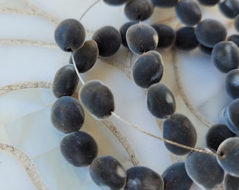 May include: A strand of dark gray, oval-shaped beads strung on a thin silver wire. The beads are smooth and have a slightly textured surface.