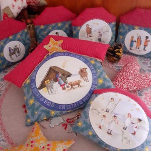 Könnte beinhalten: Ein Set an Weihnachtskissen mit verschiedenen Szenen aus der Weihnachtsgeschichte. Die Kissen sind mit blauem und rotem Stoff verziert und zeigen einen Stern, eine Kuh, einen Esel und eine Krippe. Der Text "Gloria in Excelsis Deo" ist auf den Kissen gedruckt.