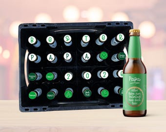 May include: A black plastic beer crate filled with beer bottles, each with a white and green bottle cap. One bottle stands upright with a green label that says "Papa" and "Alles liebe zum Vatertag! Hab dich lieb!"