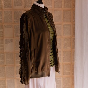 May include: A brown bomber jacket with ruffled sleeves. The jacket is on a mannequin and has a zipper closure.