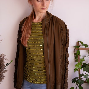 May include: A brown bomber jacket with ruffled sleeves and a gold sequined top underneath.
