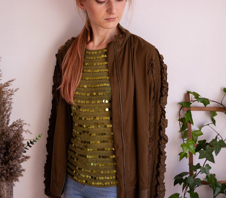 May include: A brown bomber jacket with ruffled sleeves and a gold sequined top underneath.