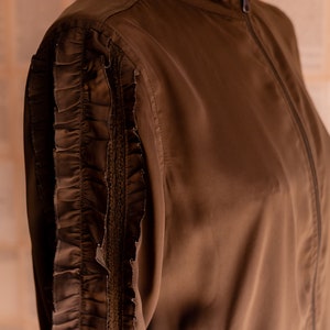 May include: A brown jacket with a zipper closure and a ruffled detail on the sleeves.