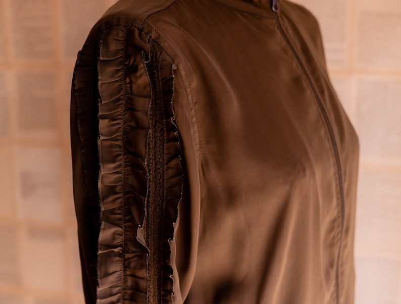 May include: A brown jacket with a zipper closure and a ruffled detail on the sleeves.