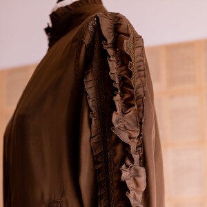 May include: A brown long-sleeved blouse with a high collar and ruffles on the sleeves.