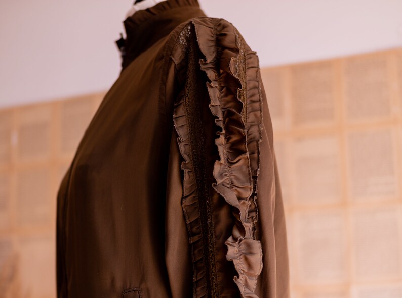May include: A brown long-sleeved blouse with a high collar and ruffles on the sleeves.