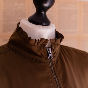May include: A brown jacket with a ruffled collar and a zipper closure.