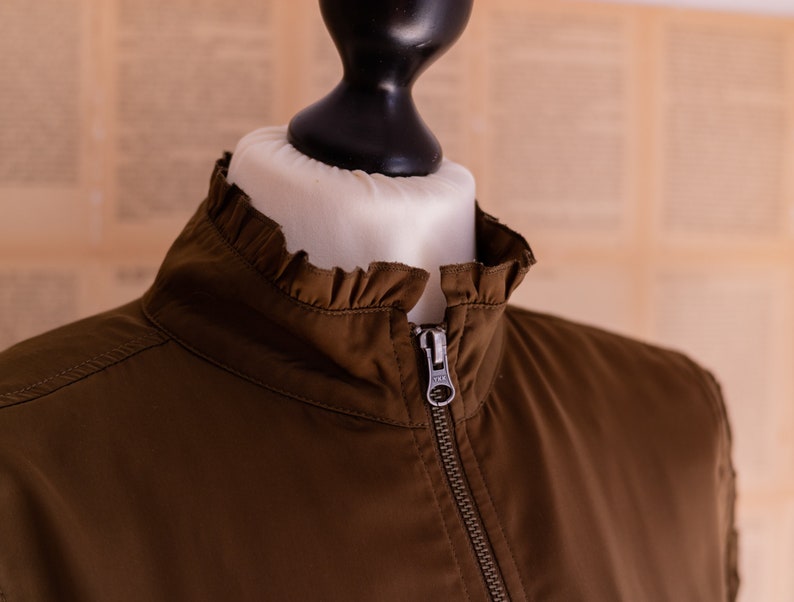 May include: A brown jacket with a ruffled collar and a zipper closure.