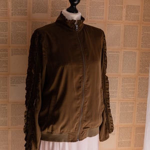 May include: A brown bomber jacket with ruffled sleeves. The jacket has a zipper closure and a ribbed hem.