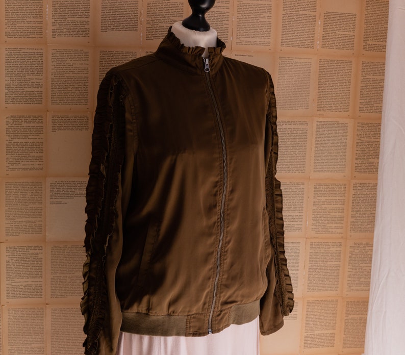 May include: A brown bomber jacket with ruffled sleeves. The jacket has a zipper closure and a ribbed hem.
